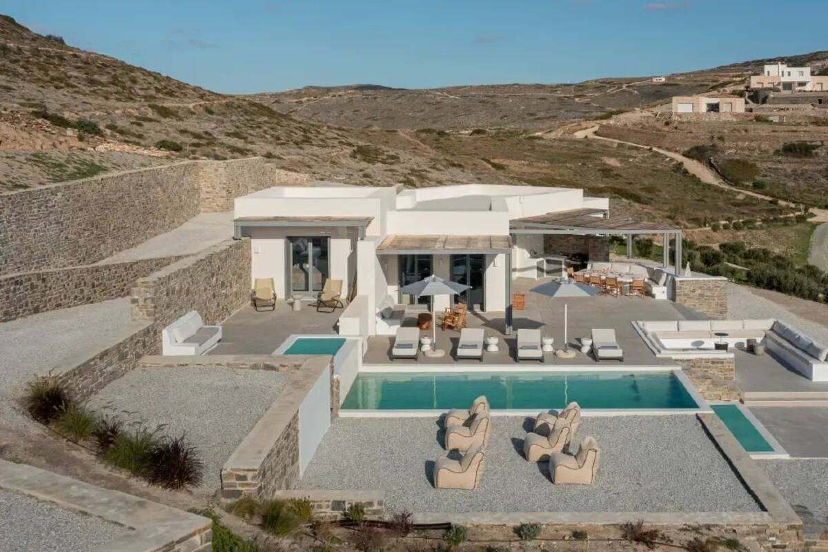 A modern villa with a swimming pool, outdoor seating, and a view of the surrounding landscape.