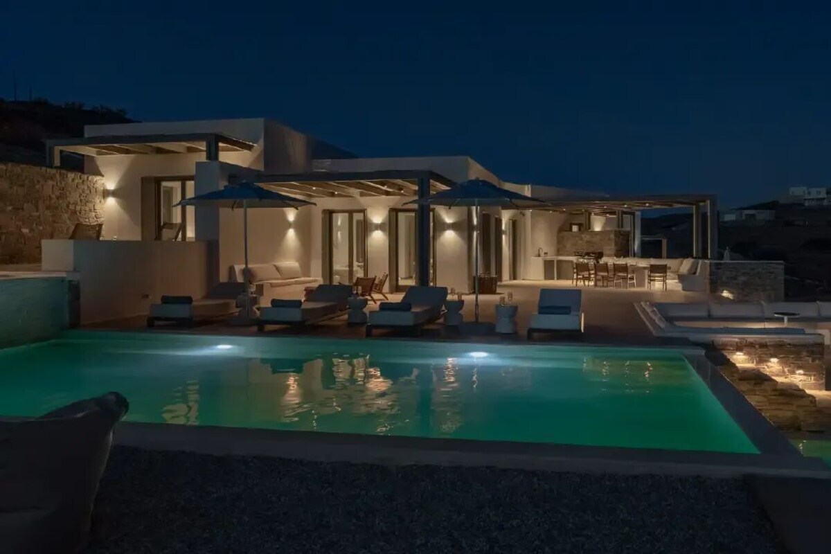 Una villa moderna con piscina, mobiliario exterior y un patio bien iluminado.