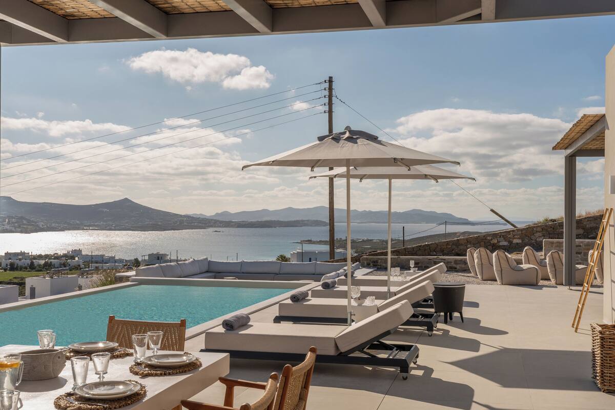 A poolside area with a table set for dining, lounge chairs, and an umbrella.