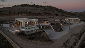 A modern resort with multiple buildings, outdoor seating areas, and a swimming pool. - Avera Luxury Private Villas (Paros)