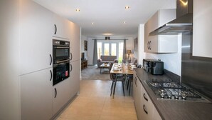 A modern kitchen with built-in appliances, a dining area with a table and chairs, and a living room with a sofa and a TV. - A stunning new build property (Cheshire West and Chester)