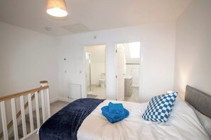 A bedroom with a bed, a blue towel, and a checkered pillow. There is a white radiator and a wooden staircase. - A stunning new build property (Cheshire West and Chester)