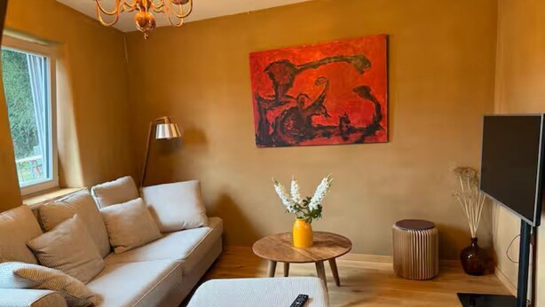 Ein Wohnzimmer mit Sofa, Hocker, rundem Tisch und einem Bild an der Wand.