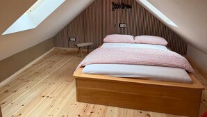 Ein Schlafzimmer mit schräg stehender Decke, Holzboden, einem Bett mit gestreifter Bettwäsche und einem kleinen Tisch.