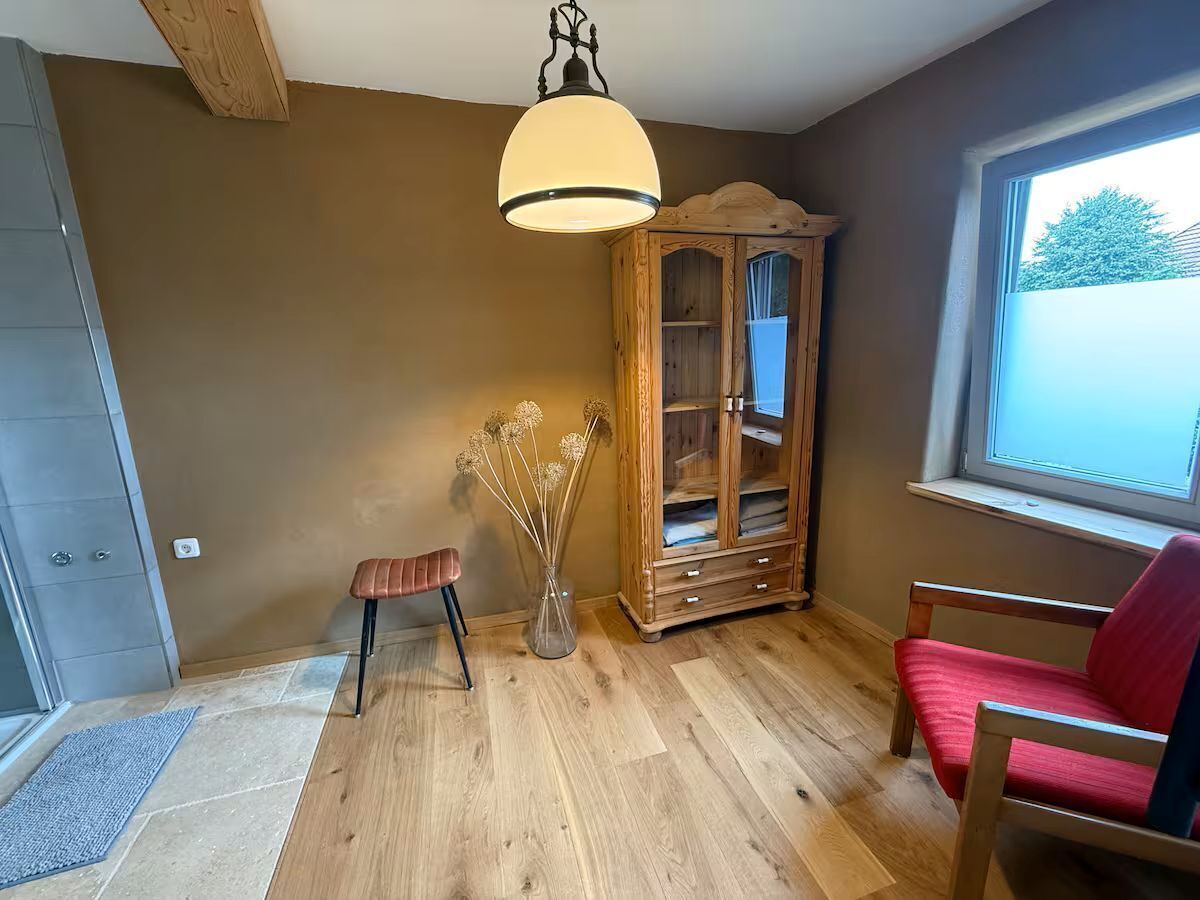 Una habitación con suelo de madera, una silla roja, un armario de madera y una lámpara colgante.