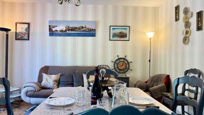 Un coin repas avec une table dressée pour deux personnes, un canapé et un mur décoratif orné de tableaux encadrés.