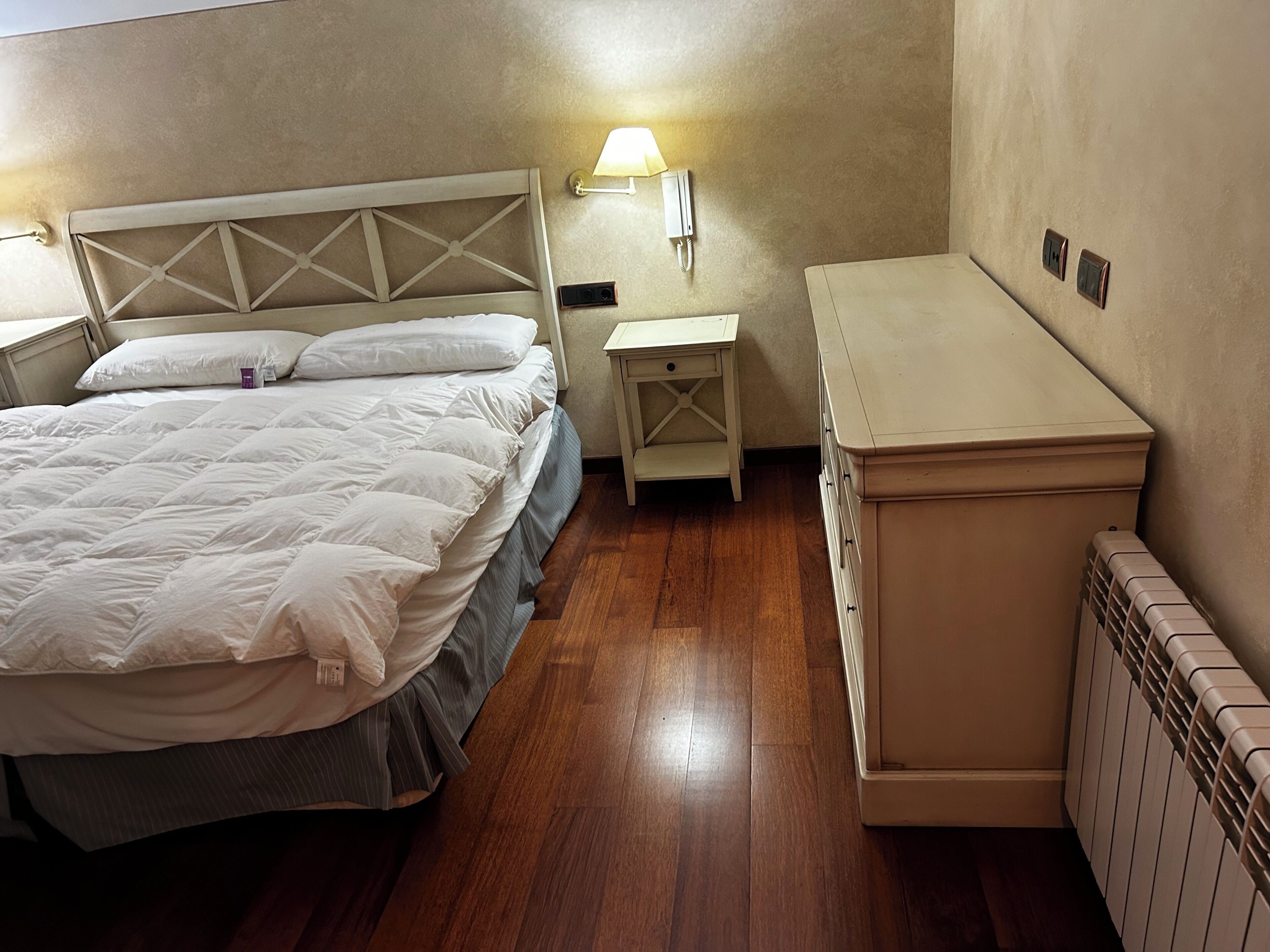 Een slaapkamer met een bed, nachtkastje, lamp en radiator.