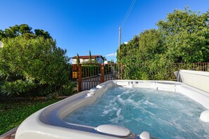 A hot tub surrounded by lush greenery and a house in the background. - MGH- Dajaami Apartment Lazise (Lazise)