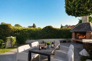 Un patio al aire libre con una mesa, sillas, una barbacoa de ladrillo y un seto al fondo.