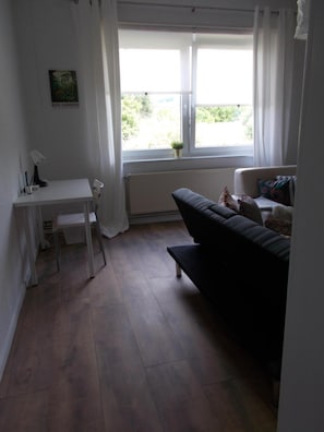 A small, bright room with a white desk, a black sofa, and a window with curtains. - Nature and Tranquility Surrounded by Gentle Hills and Evergreen Fields – Perfect for Peace Seekers (Uslar)