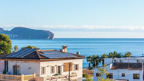 Un edificio sul lungomare con pannelli solari, un cartello con scritto "RESTAURANT" e vista sul mare e un'isola in lontananza.