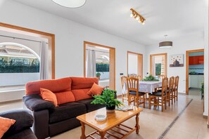Una sala de estar moderna con sofá, mesa de comedor y sillas, ventanas amplias y vistas al exterior.