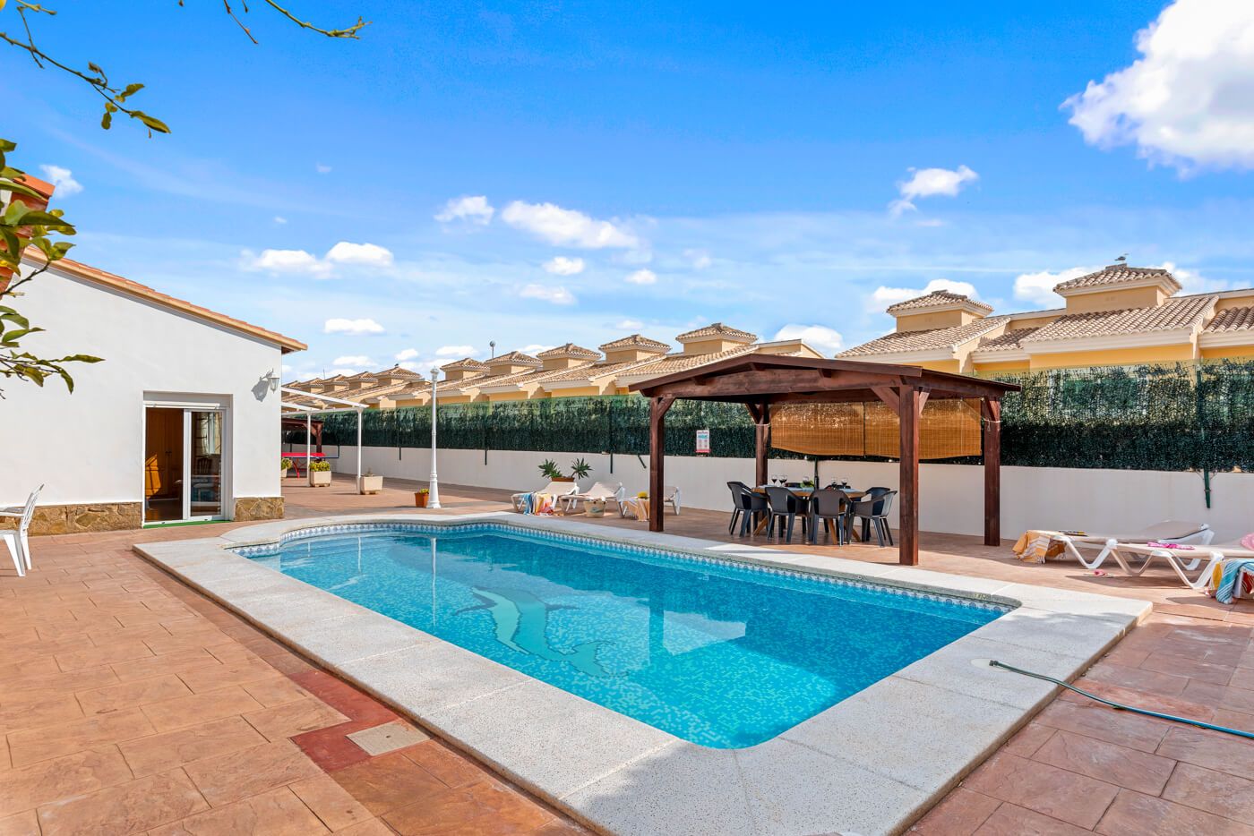 Una piscina con una pérgola de madera, sillas de descanso y un área de comedor cubierta.