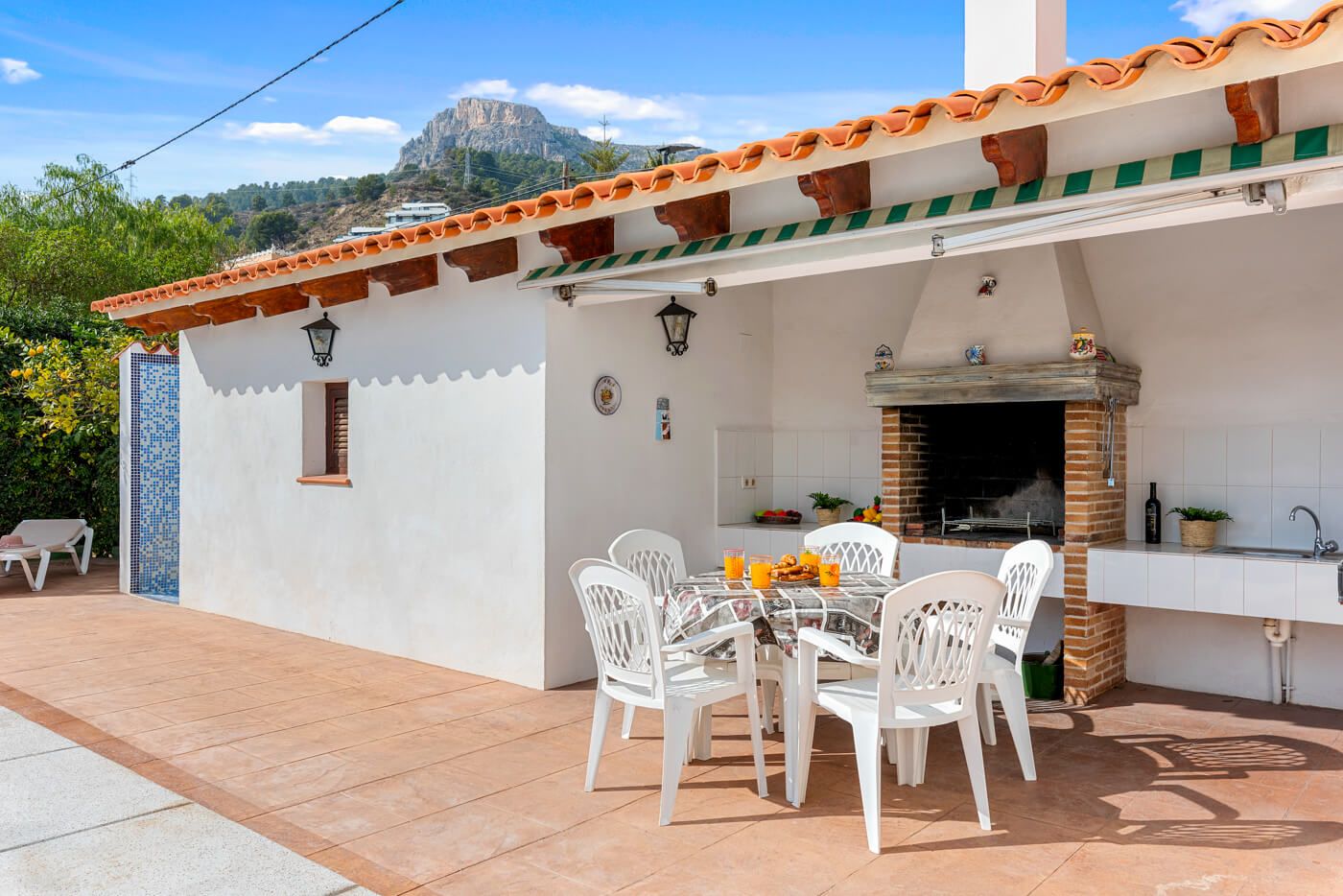Eine Terrasse im Freien mit Esstisch und Stühlen, einem Backofen aus Ziegelsteinen und einer weißen Küchenzeile.