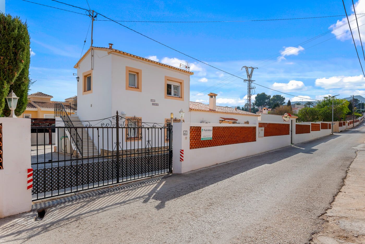 Una propietat tancada amb un edifici blanc, una reixa metàl·lica i un mur de maó.