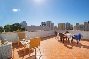 An outdoor terrace with a table set for dining, chairs, and a view of a cityscape with buildings and a mountain in the distance. - Villa Flora - Plusholidays (Calpe)
