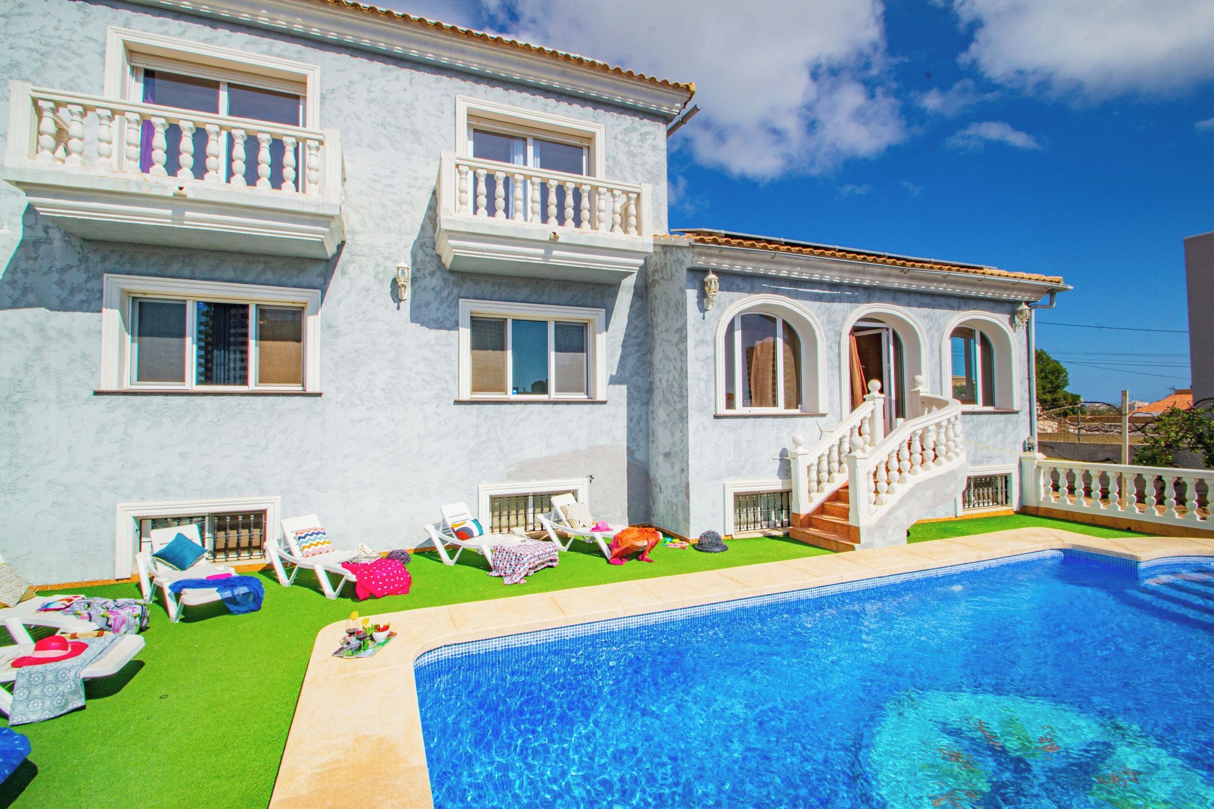 A two-story building with a swimming pool, multiple windows, and a staircase leading to a balcony.
