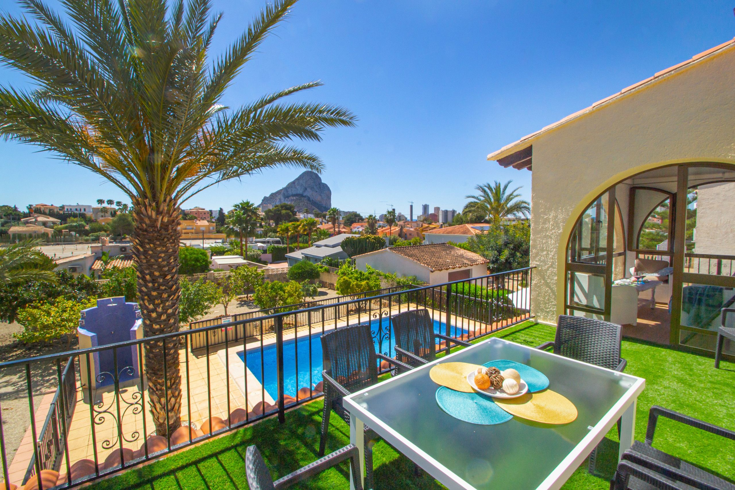 A balcony with a pool, outdoor furniture, and a view of a cityscape with a prominent rock formation.