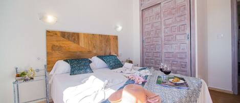 A hotel room with a bed, a bedside table, a wardrobe, and a dining area with a table set for two.