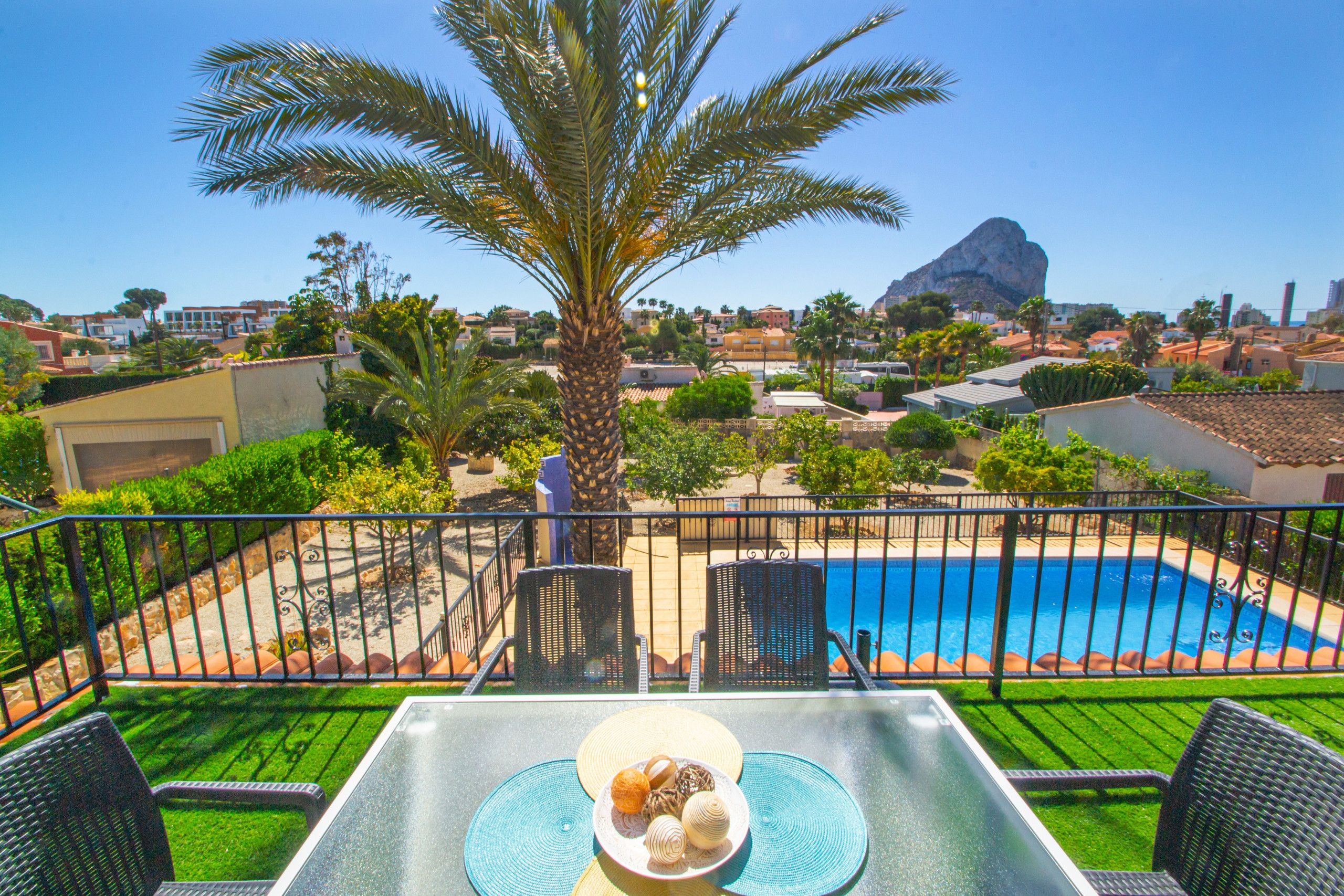 Een balkon met uitzicht op een zwembad, palmbomen en een berg op de achtergrond.