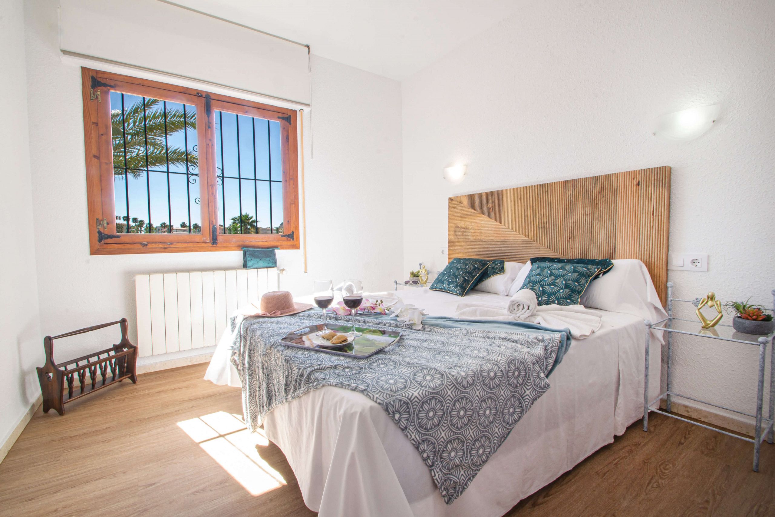 A bedroom with a bed, a window, a radiator, a bedside table, and a wall-mounted light fixture.