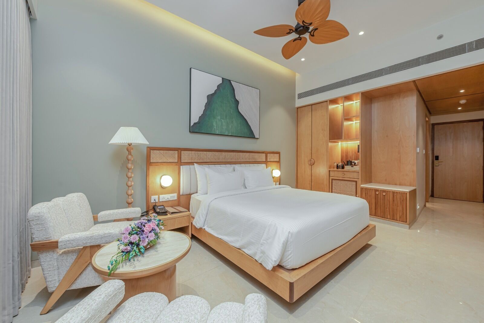Una habitación de hotel con cama, mesita de noche, lámpara, silla y ventilador de techo.