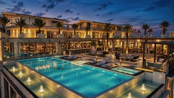 A multi-level hotel with a large outdoor swimming pool, lounge areas, and palm trees.
