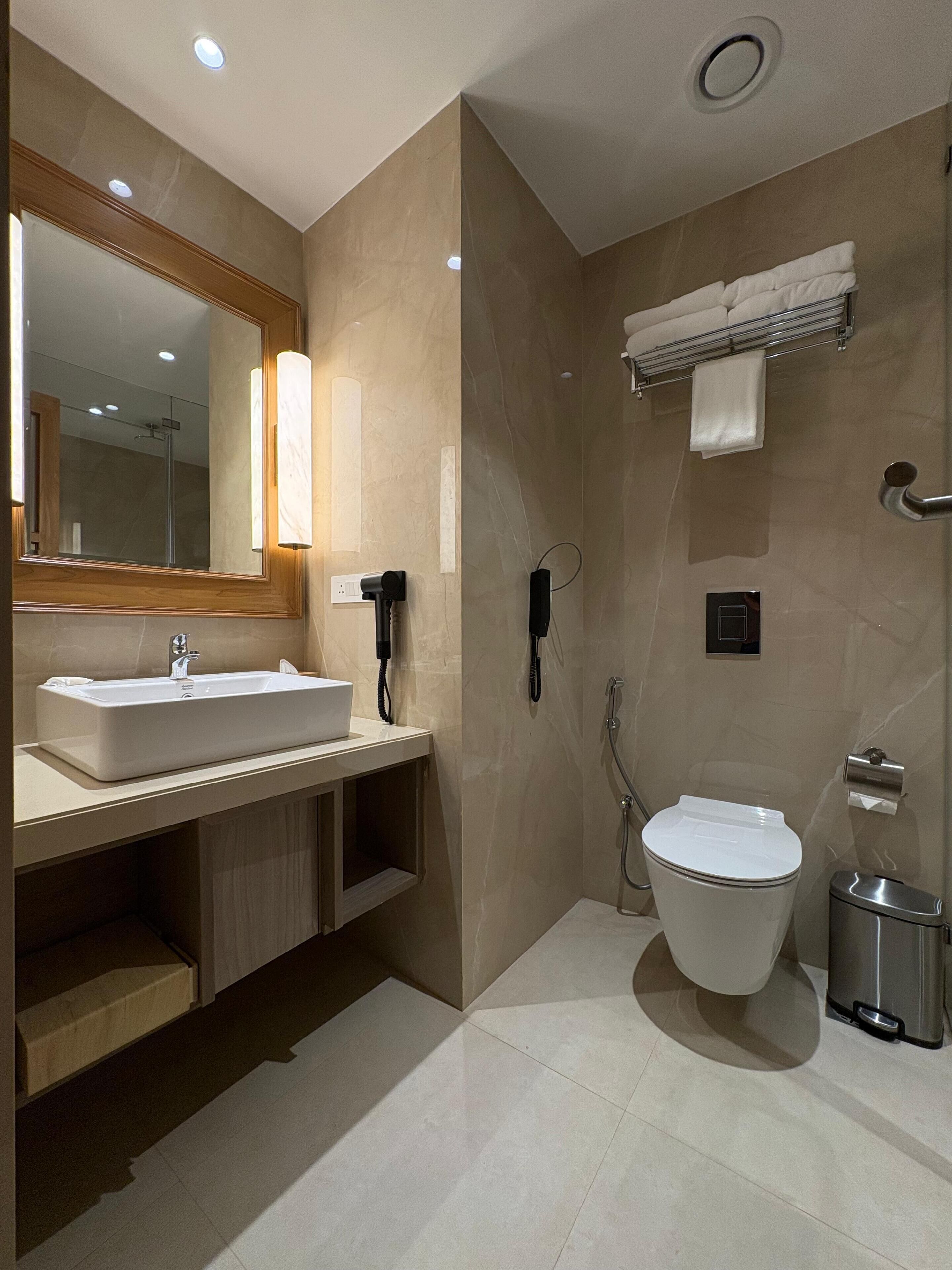 A modern bathroom with a large mirror, a sink, a toilet, and a shower.
