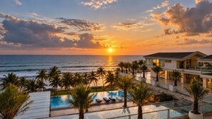 Un resort con piscina, palme e vista sull'oceano al tramonto.