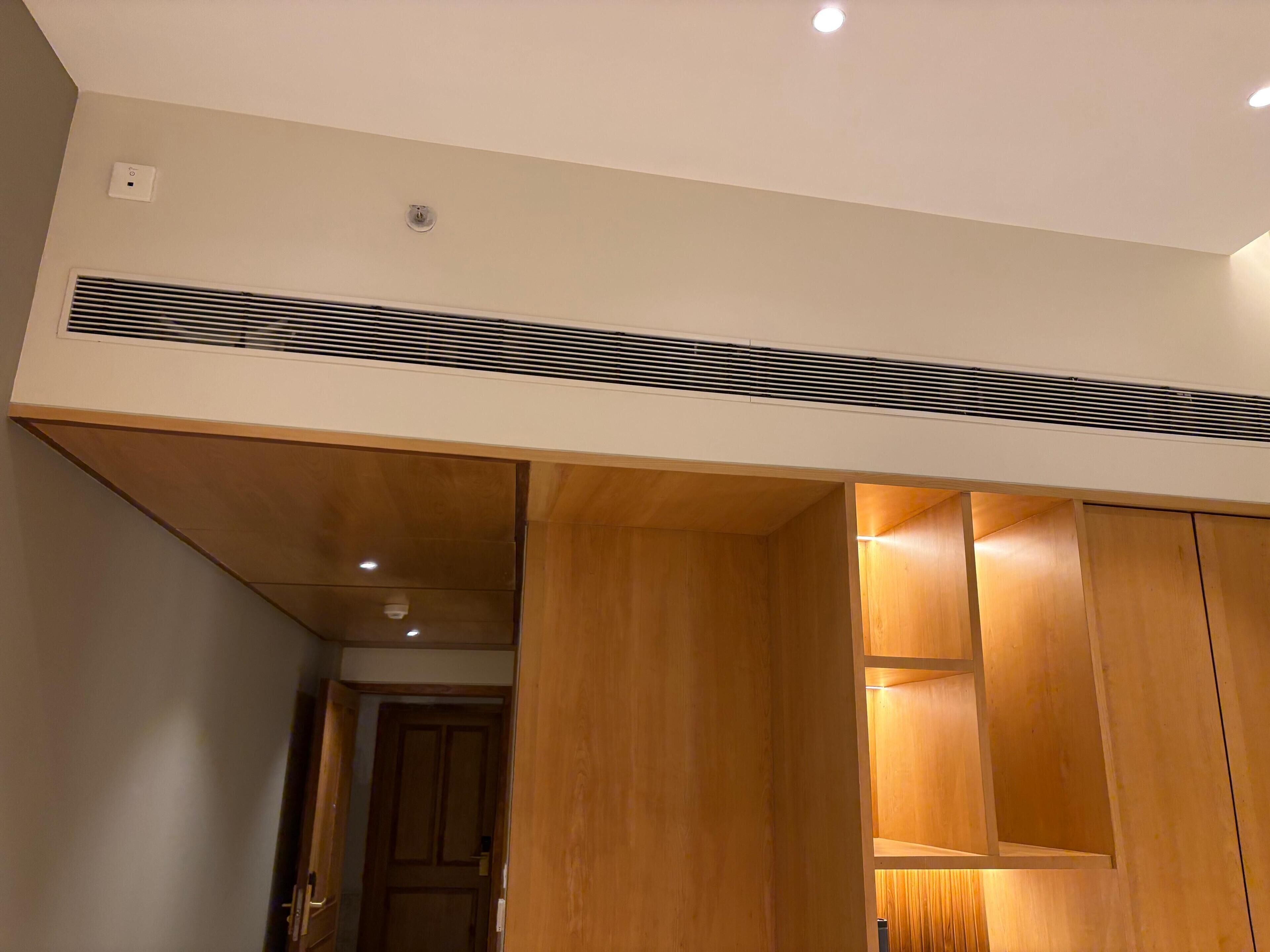 Una habitación con un armario de madera, un respiradero en el techo y una puerta que da a otra estancia.