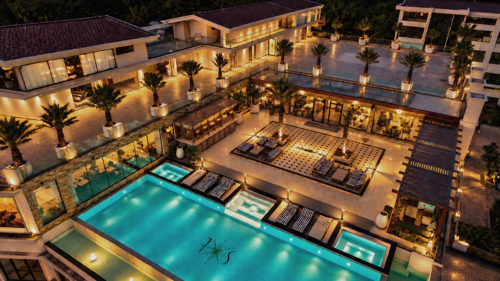 Un hotel de varios niveles con una amplia piscina, zonas de estar al aire libre y palmeras.