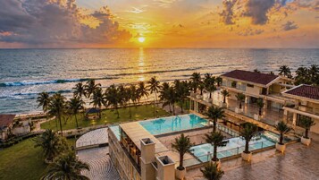 Un resort con piscina, palmeras y vistas al océano al atardecer.