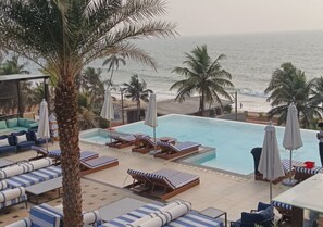 A poolside area with lounge chairs and umbrellas, overlooking the ocean. - Peninsula Del Mar Beach Resort (Udupi)
