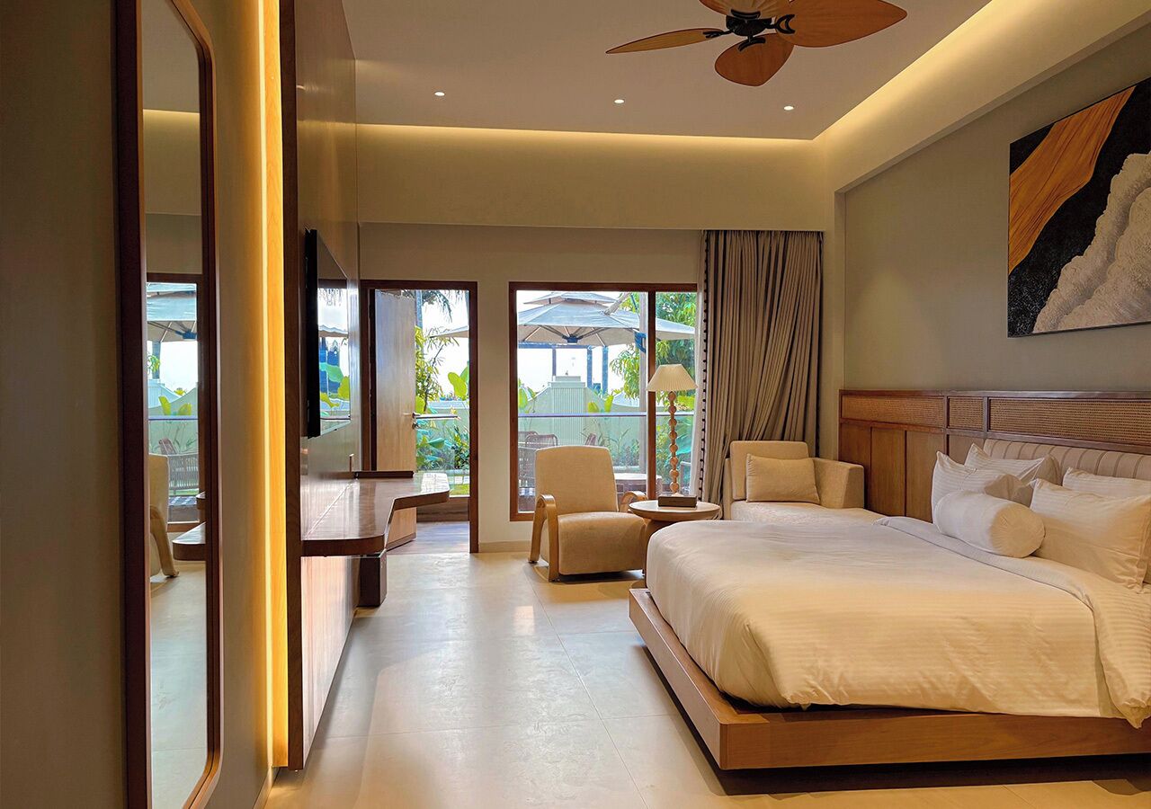 A modern hotel room with a large bed, a sitting area with a chair and table, and a view of the outdoors.