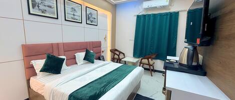 A hotel room with a bed, a desk, a chair, a ceiling fan, and framed pictures on the wall.