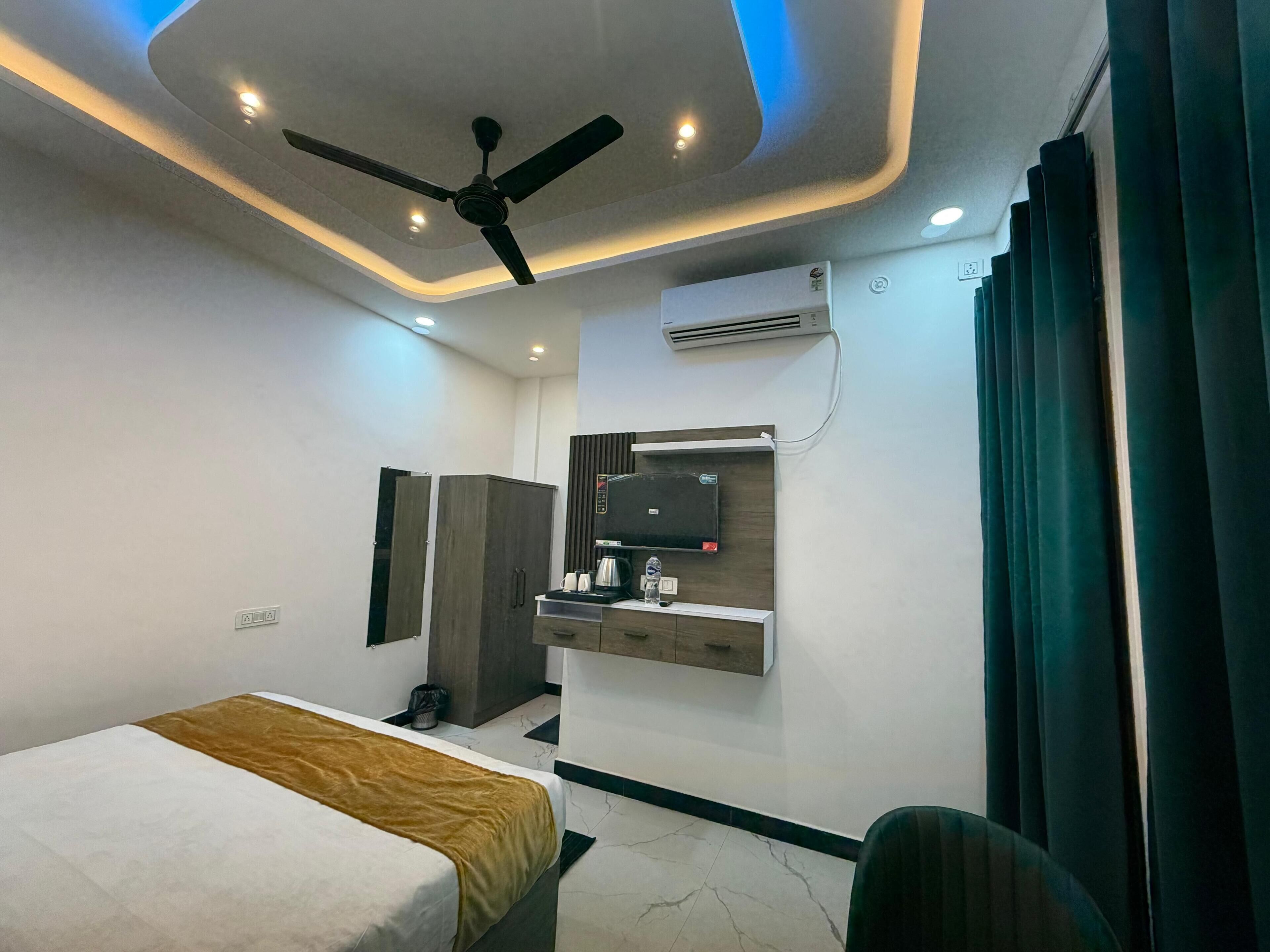 A hotel room with a bed, a desk with a mirror, an air conditioning unit, and a ceiling fan.