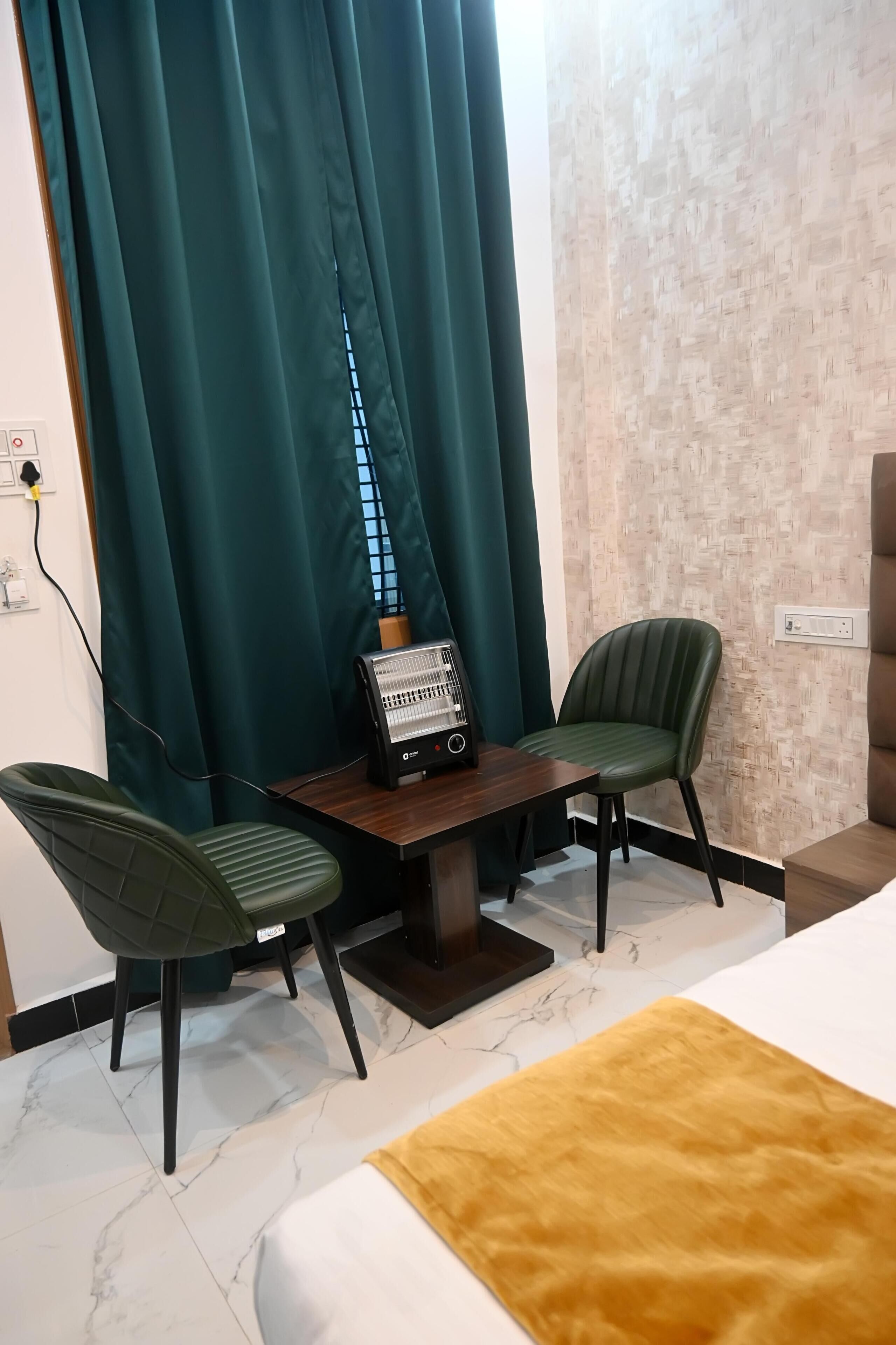 A hotel room with a bed, a desk with a heater, two chairs, and a window with curtains.