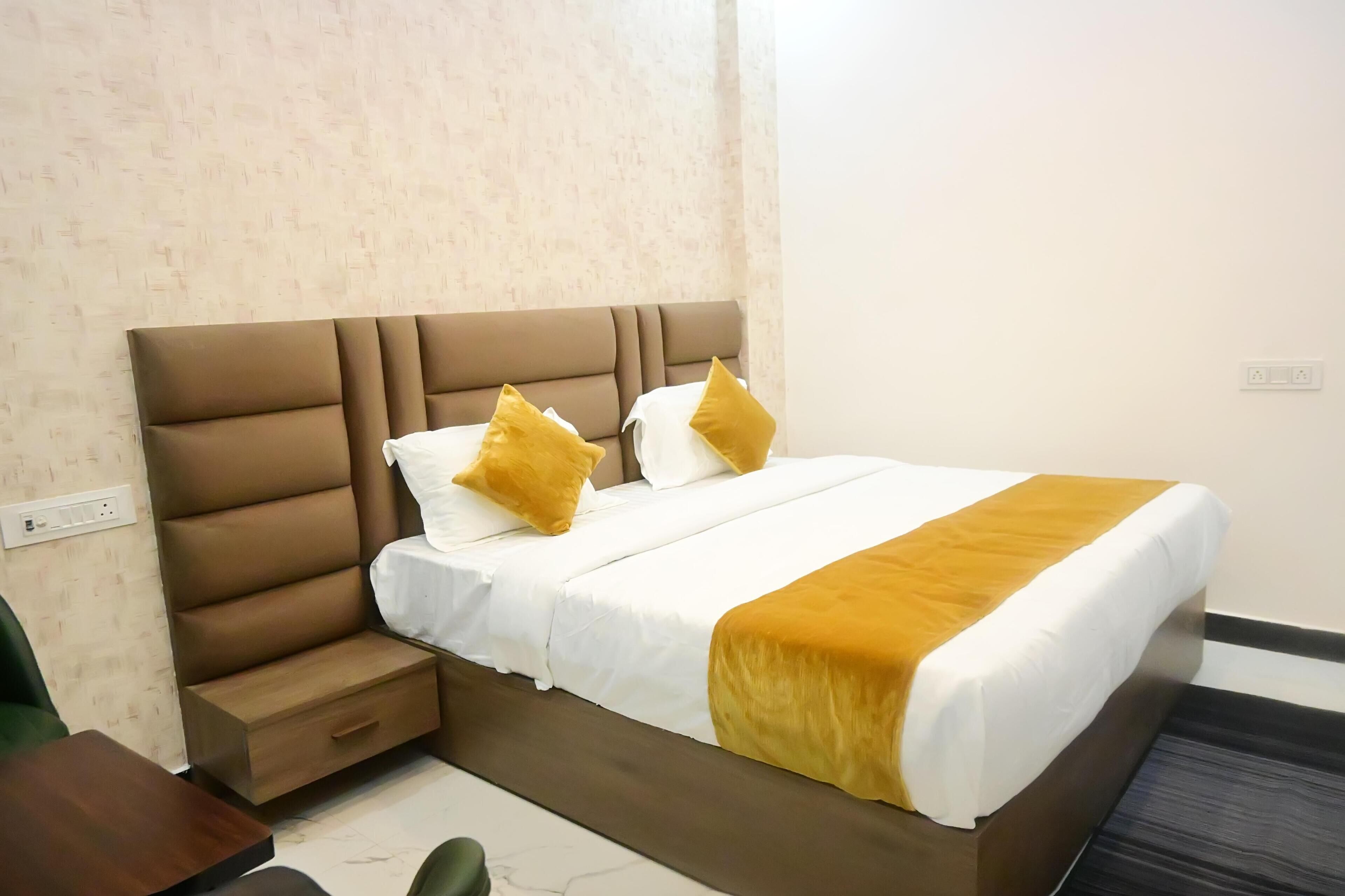Una cama bien hecha con cabecera marrón, ropa de cama blanca y dos almohadas amarillas.