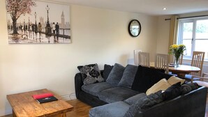 A living room with a grey sofa, a wooden coffee table, and a painting of a cityscape. -  Cosy warm cottage Cirencester,Capital of the Cotswolds,bibury close pet frendly (Cirencester)