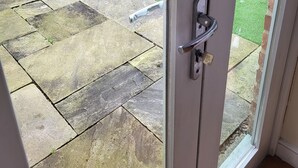 A view through a glass door into a patio area with a stone floor and a wooden fence in the background. -  Cosy warm cottage Cirencester,Capital of the Cotswolds,bibury close pet frendly (Cirencester)