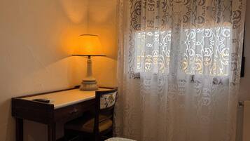 Una habitación con un escritorio de madera, una lámpara y una ventana con cortinas estampadas.