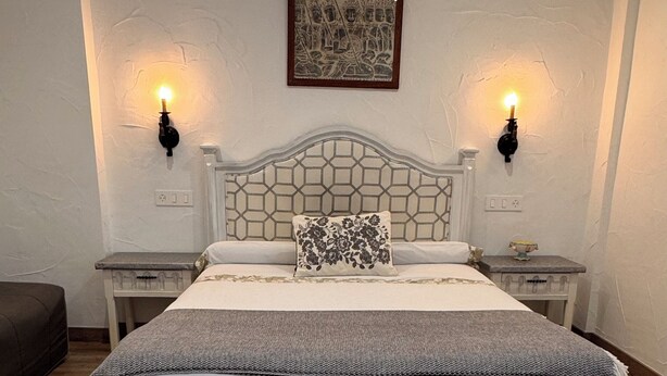 Een net opgemaakt bed met een wit hoofdeinde, twee nachtkastjes met lampen en een ingelijst plaatje aan de muur.