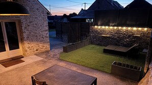 Un patio con mesa y sillas, un muro de piedra y un pequeño césped.