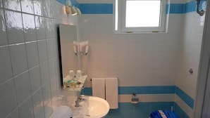 Une salle de bain équipée d’un lavabo, de toilettes et d’une baignoire. On y trouve un porte-serviettes avec une serviette, un miroir et une fenêtre au-dessus du lavabo.