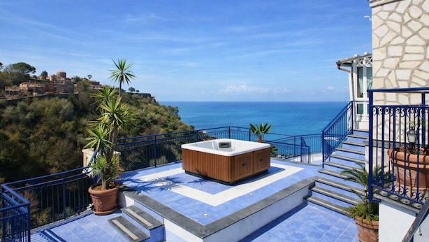Un balcon doté d’un jacuzzi, de quelques marches et offrant une vue sur la mer et une ville historique.
