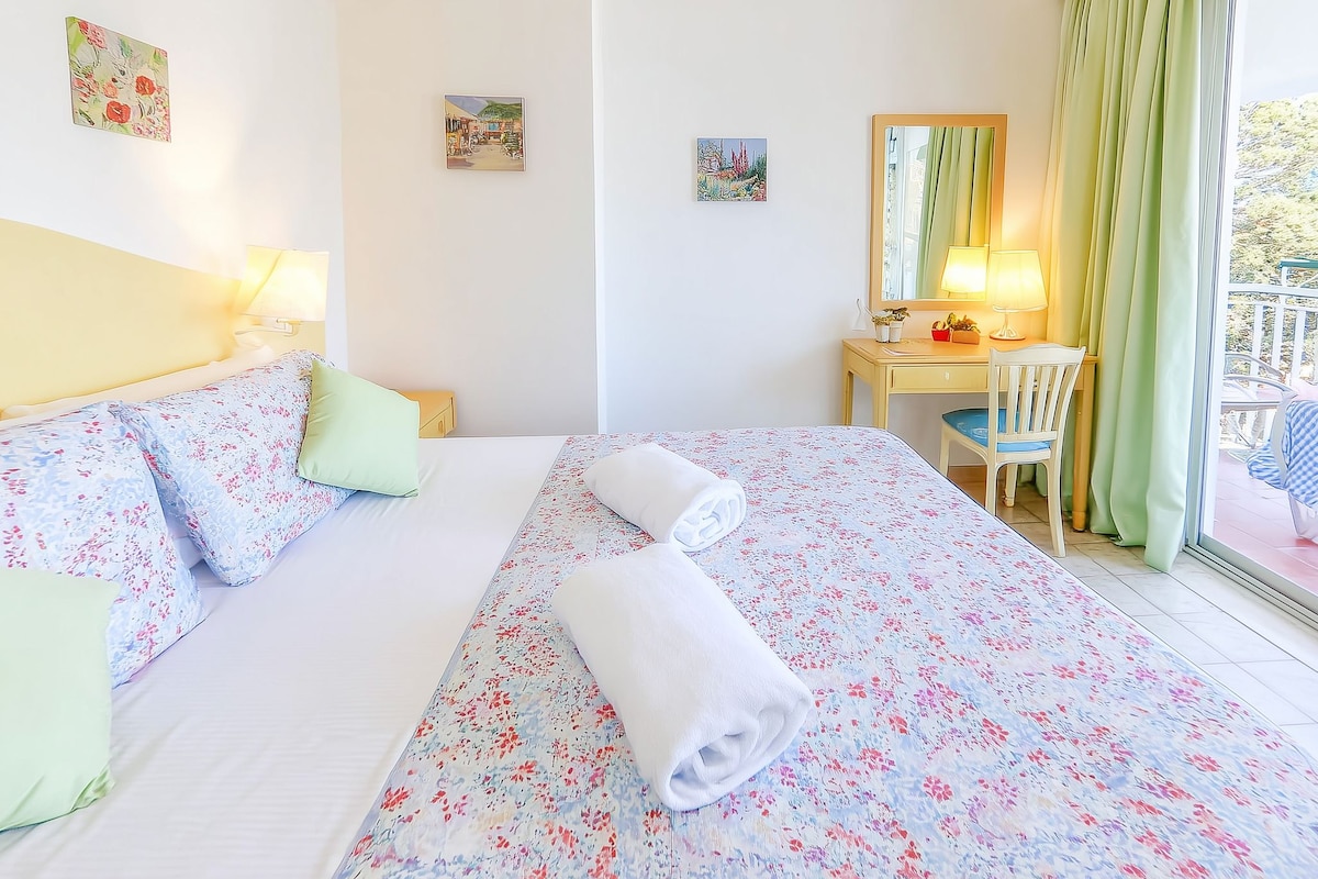 Una habitación de hotel con cama, escritorio, silla y ventana con cortinas.