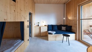 Une pièce en bois avec un lit, une petite table sur laquelle est posée une plante, et une fenêtre.