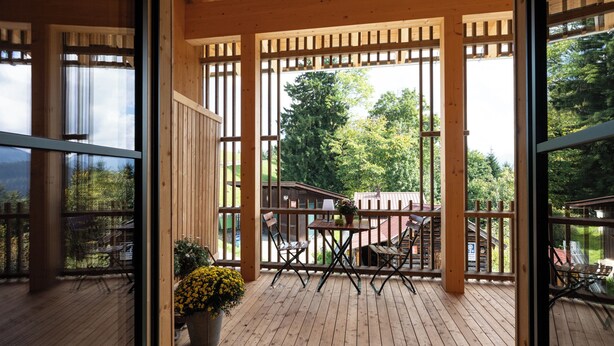 Une terrasse en bois agrémentée d’une pergola, de sièges d’extérieur et offrant une vue sur un chalet en arrière-plan.