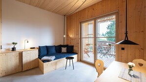 Un intérieur moderne avec un plafond en bois, un canapé-lit, une table à manger et une grande fenêtre donnant sur le mobilier d’extérieur.