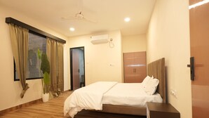 A bedroom with a bed, a ceiling fan, an air conditioning unit, wooden flooring, and a window with curtains. - Dornix by Housiify (Gurugram)